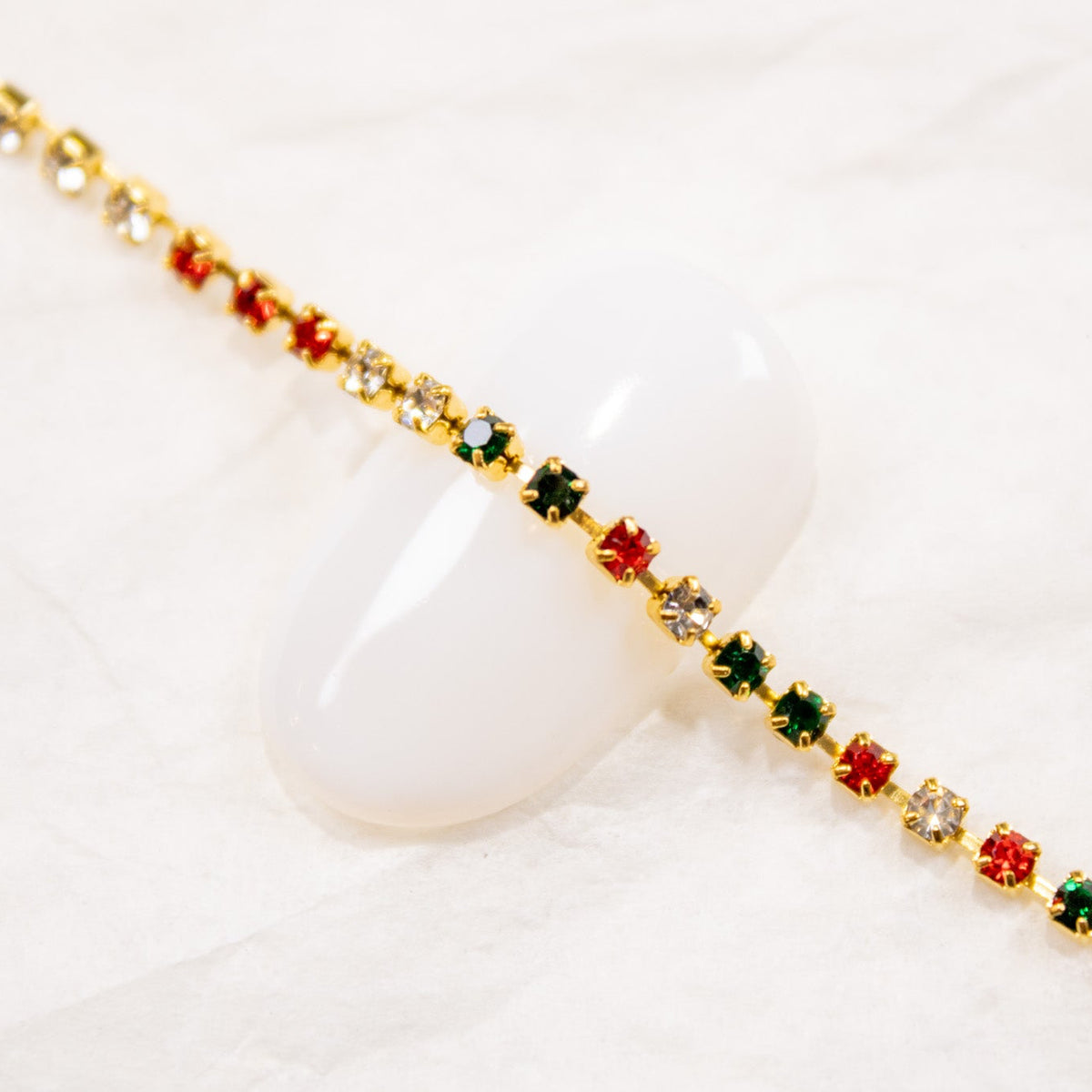 Angled shot of red, green, and crystal gem chain for nail art laid out on a white surface.