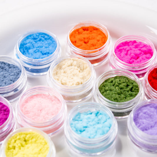 Top-down view of 12 open jars displaying bright and pastel velvet flocking nail powders.