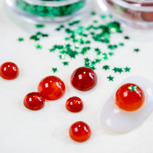 Red tomato nail charms paired with green star glitters arranged on a white background.