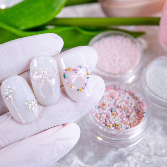 Hand holding three false nails featuring pink gel designs styled with tiny 0.8mm micro pearl beads and bow accents.