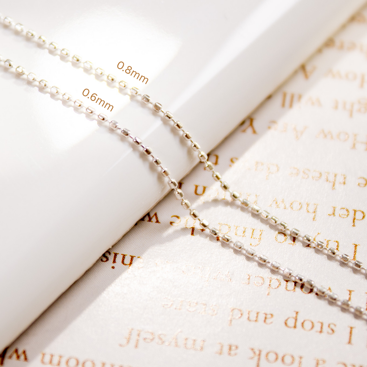Close-up view of 0.6mm and 0.8mm silver bead chains draped over a white dish.