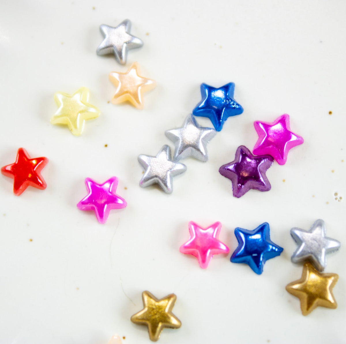 Colorful metallic and pearlescent star nail charms scattered across a white surface