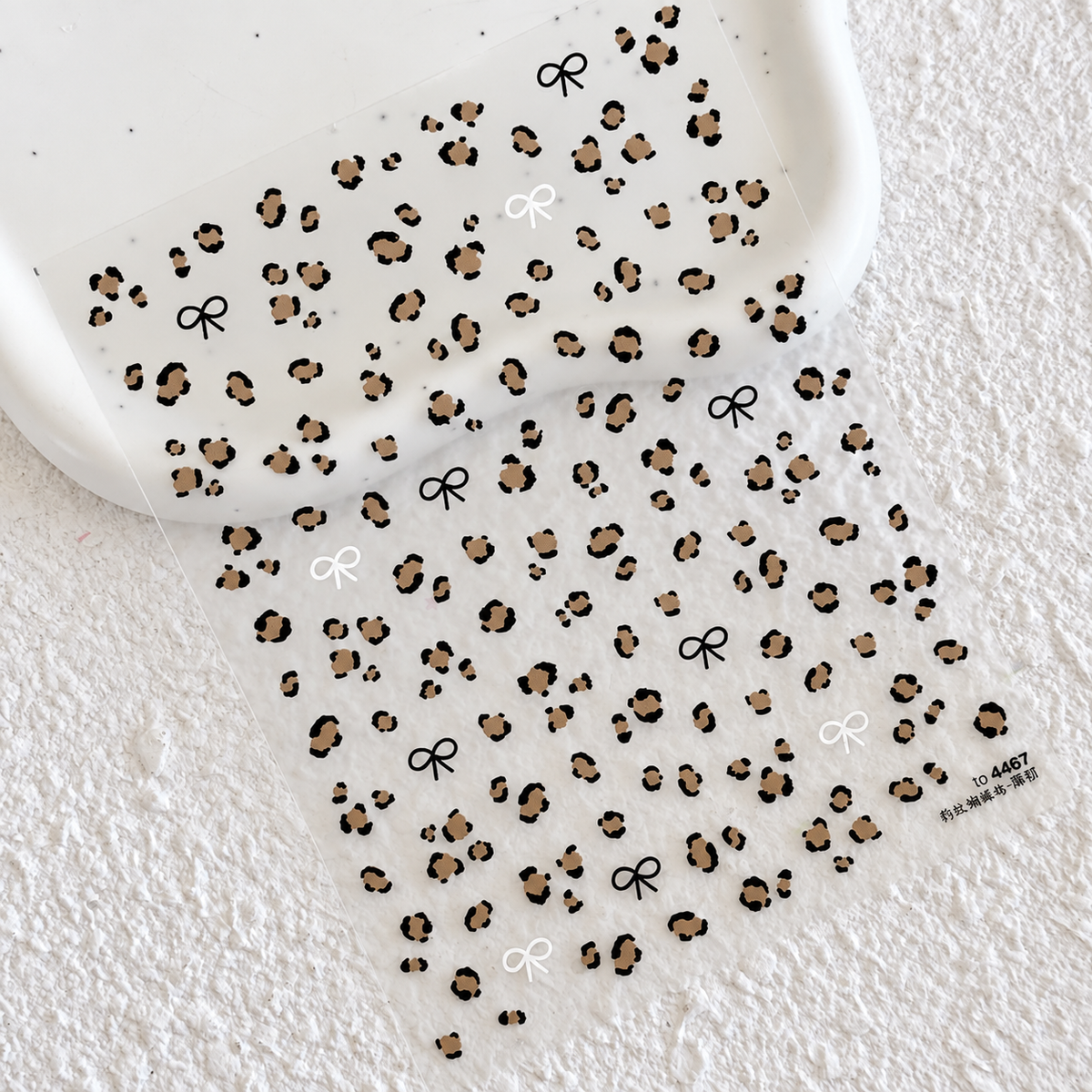 Full sheet of leopard print nail stickers featuring classic brown leopard spots and black and white mini bow accents on a scalloped ceramic tray.