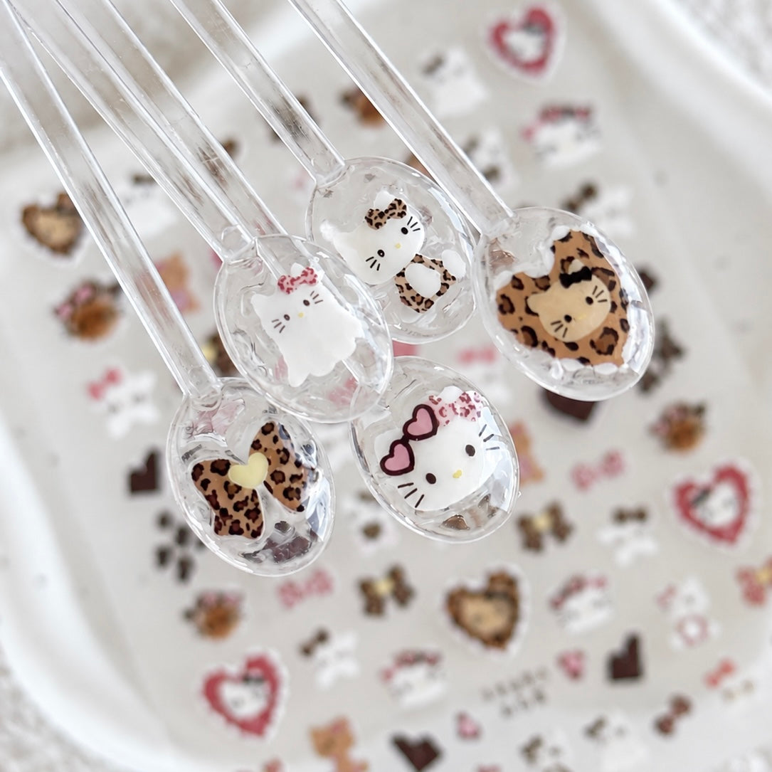 Clear press-on nail swatches decorated with leopard kitty head and pink bow nail art stickers placed over the sticker sheet.