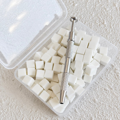 Silver metal sponge grabber tool resting on top of a clear plastic storage container filled with 100 white mini nail art sponges.