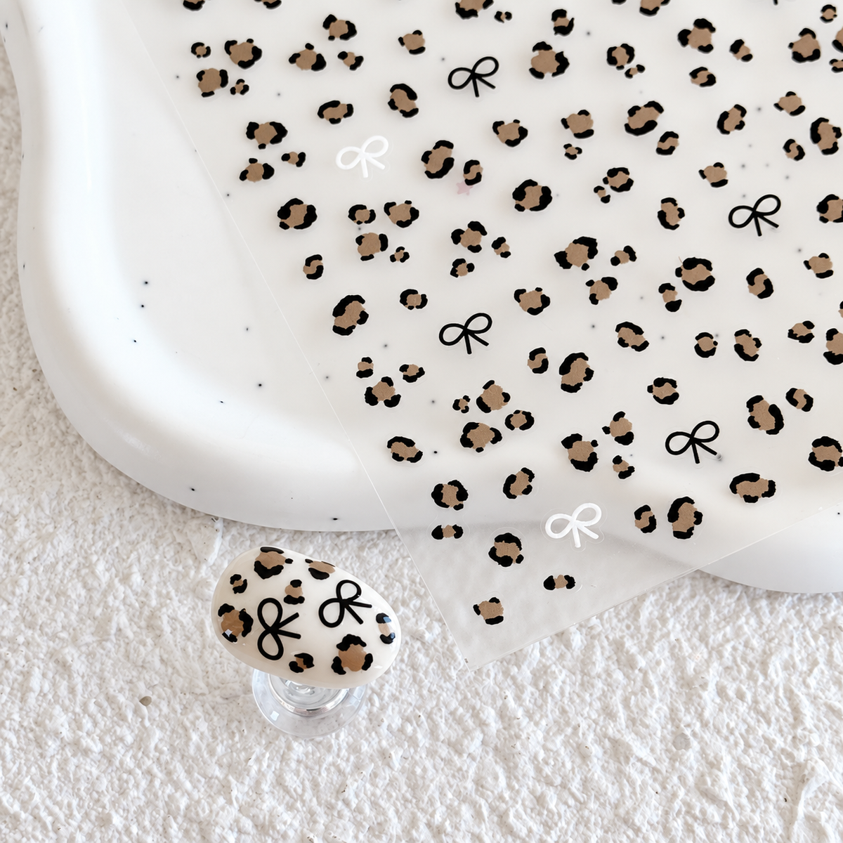 Leopard print nail sticker sheet resting on a white ceramic dish alongside a matching leopard print press-on nail swatch.