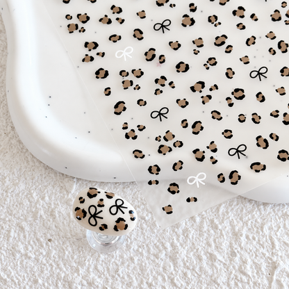 Leopard print nail sticker sheet resting on a white ceramic dish alongside a matching leopard print press-on nail swatch.