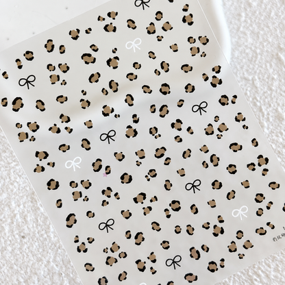 Top-down view of the entire sheet of leopard spots and black and white mini bow nail art stickers.