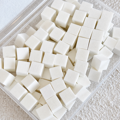 Top-down view of a clear plastic container packed with 100 small white cube-shaped mini nail art sponges.