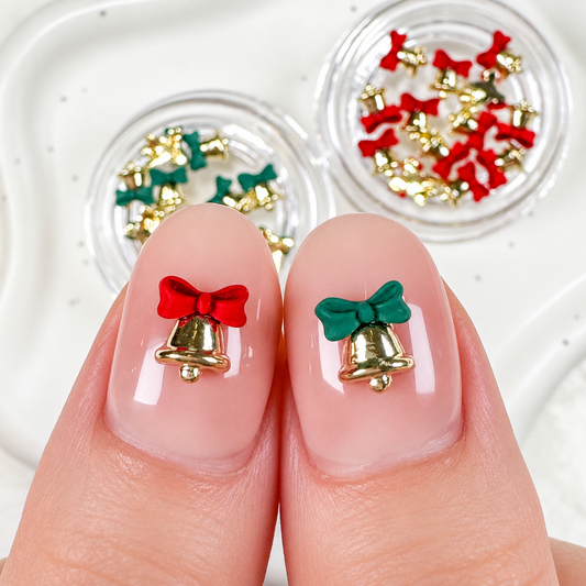 Open jars of jingle bell charms next to manicured thumbnail designs featuring 3D gold bells with red and green bows.